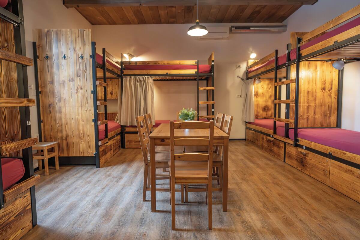 Una habitación con literas, una mesa de comedor de madera, sillas y una planta pequeña.