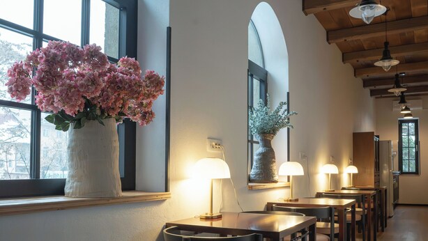 Un amplio comedor con mesas y sillas de madera, un ventanal con un jarrón de flores y un techo de madera.