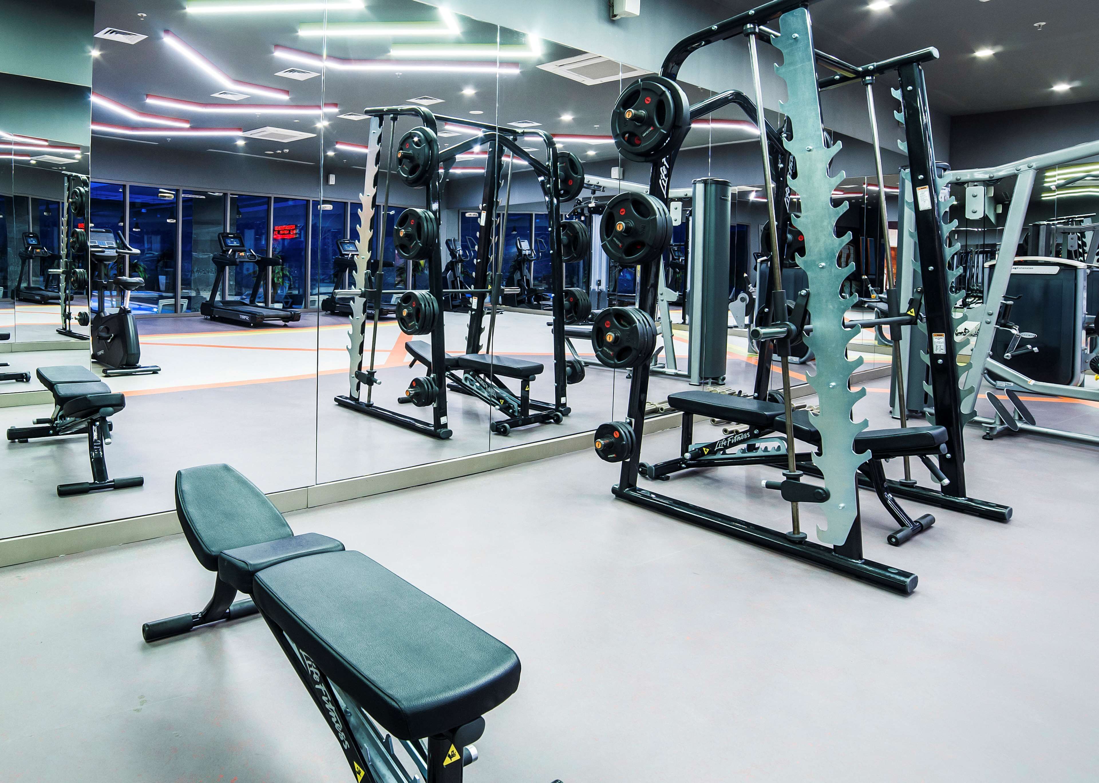 Ett gym med olika typer av styrketräningsutrustning, bänkar och speglar.