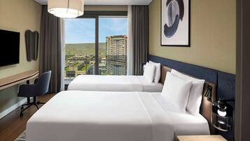 A hotel room with two beds, a desk, a chair, a TV, and a large window with a city view.