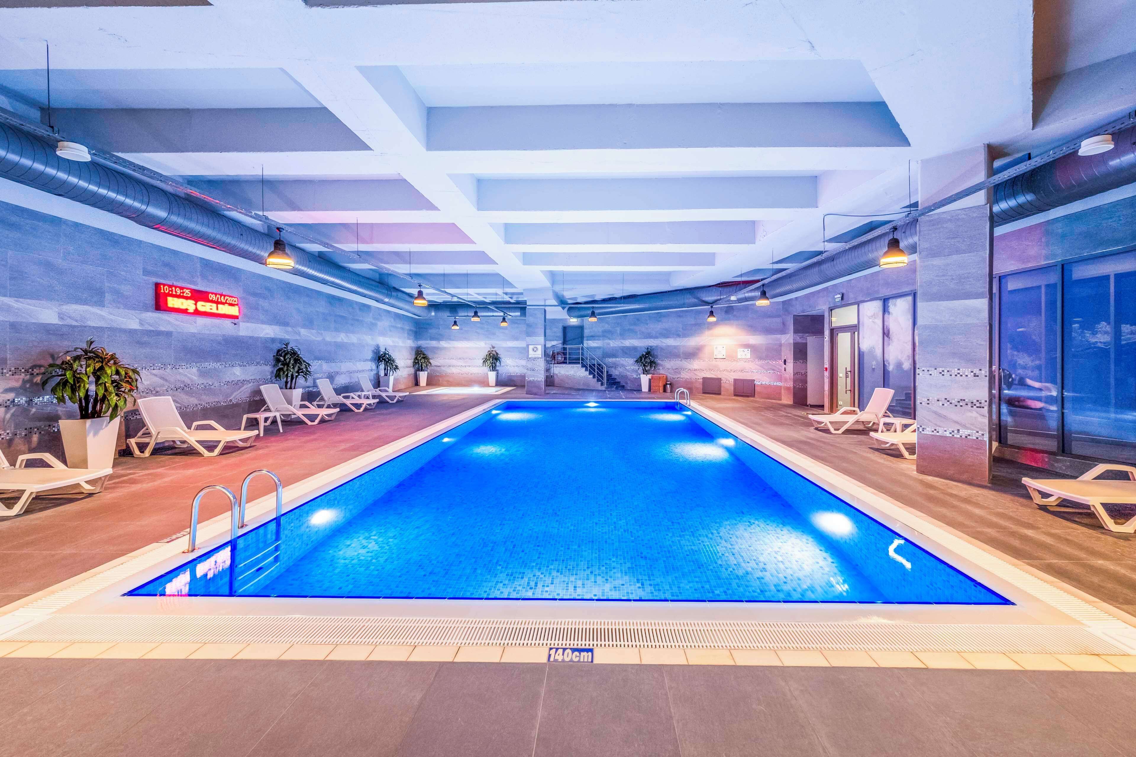 An indoor swimming pool with lounge chairs, a digital clock, and a tiled floor.