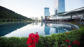 Un bâtiment moderne avec une grande piscine au premier plan, entouré de verdure et de fleurs rouges.