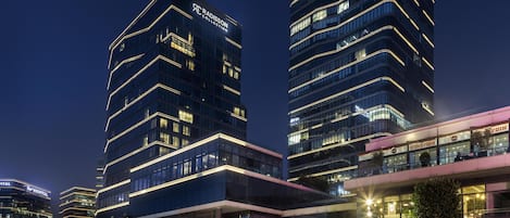 A modern hotel with a prominent Radisson Collection sign, large windows, and a visible restaurant named 'GUNAYDIN' on the ground floor.