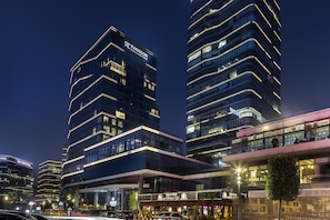A modern hotel with a prominent Radisson Collection sign, large windows, and a visible restaurant named 'GUNAYDIN' on the ground floor.