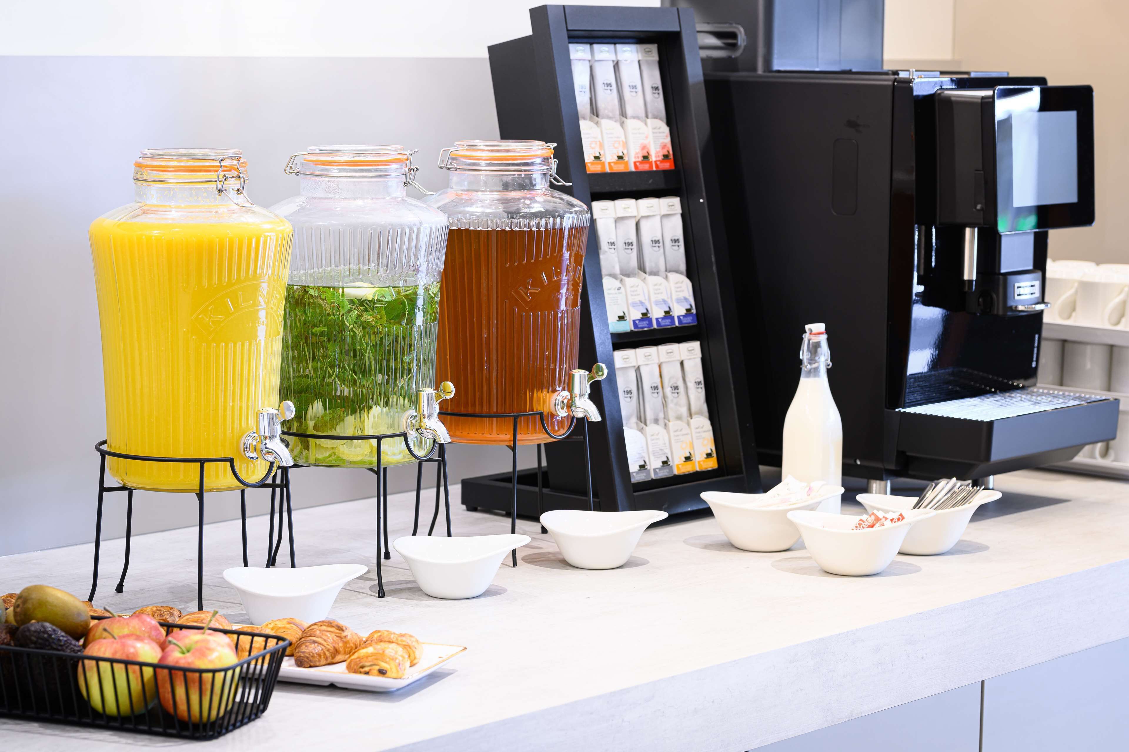 A breakfast buffet with juice dispensers, a coffee machine, and a variety of pastries and fruits.
