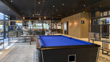 A pool table in a modern indoor setting with a bar area and seating.