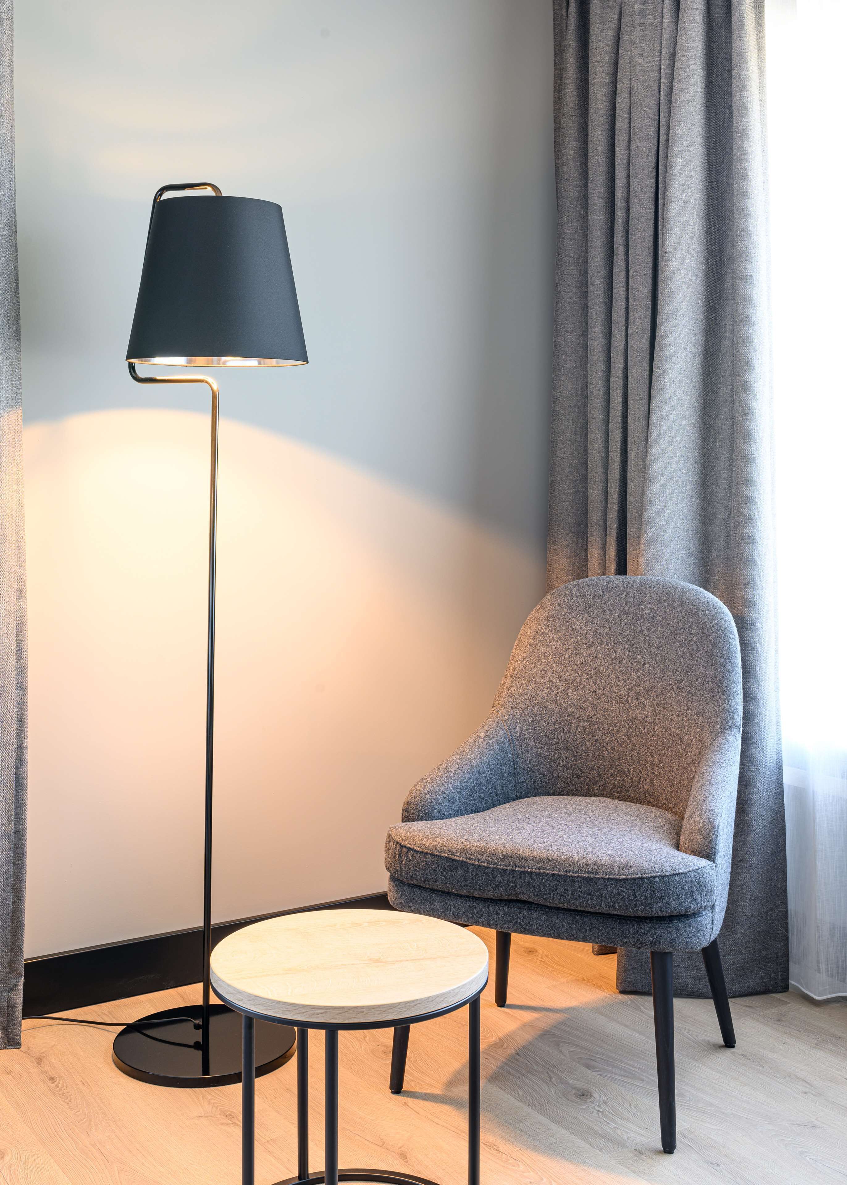 A modern room with a round table, a chair, a floor lamp, and a window with curtains.