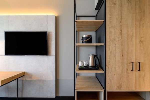 Una cocina moderna con una televisión de pantalla plana montada en la pared, armarios de madera y una encimera con una tetera y tazas.