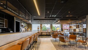 A modern bar area with a long counter, multiple bar stools, and a seating area with tables and chairs. - Radisson Hotel Antwerp Berchem (Antwerp)