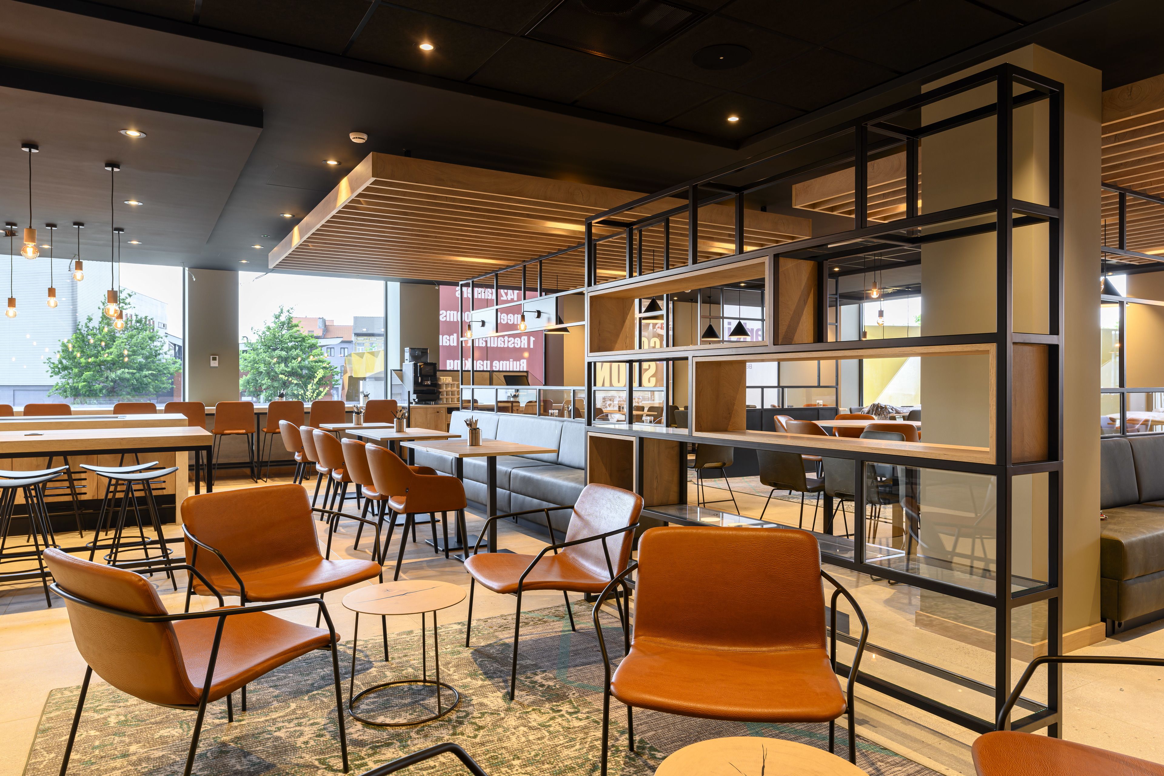 A modern cafe with orange chairs, wooden tables, and a large bookshelf.