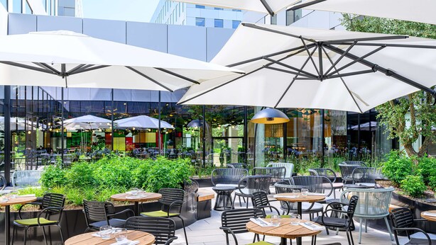 An outdoor cafe with tables and chairs, umbrellas, and greenery. - Radisson Hotel Antwerp Berchem (Antwerp)