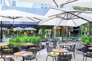 Un café al aire libre con mesas, sillas, sombrillas y plantas.