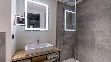 Een moderne badkamer met een grote spiegel, een witte wastafel en een douche met glazen wanden.