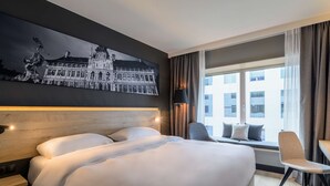 A hotel room with a large bed, a seating area with a chair and a table, a large window with curtains, and a wall-mounted artwork. - Radisson Hotel Antwerp Berchem (Antwerp)