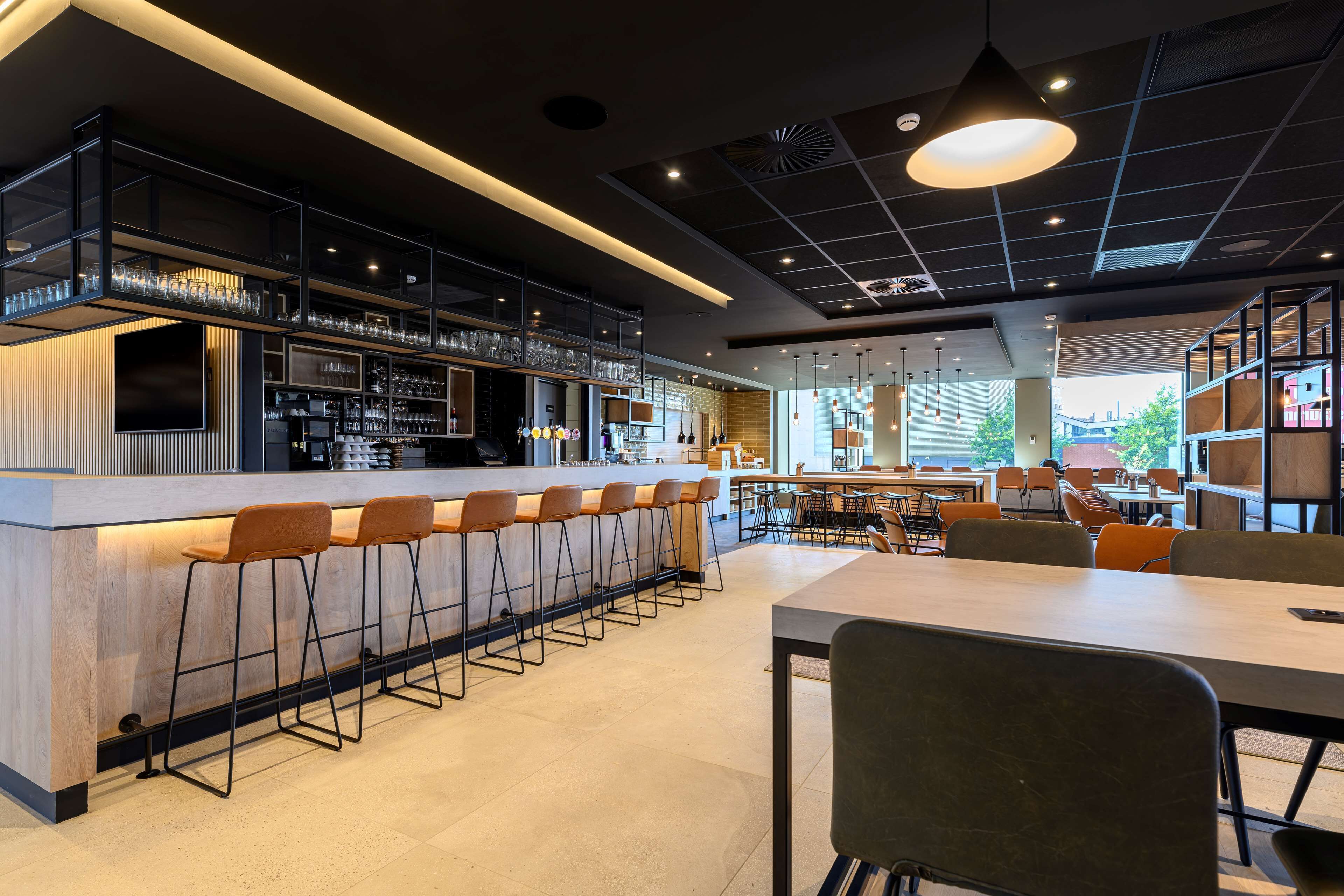 A modern bar area with a long counter, multiple stools, and a variety of glasses and bottles.