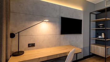 Una habitación moderna con un escritorio de madera, una lámpara de pie negra, un televisor montado y una estantería empotrada.
