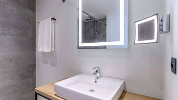 Un baño moderno con un lavabo blanco, un espejo grande y una ducha.