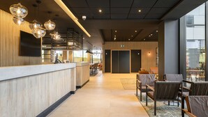 A modern hotel lobby with a reception desk, seating area, and large windows. - Radisson Hotel Antwerp Berchem (Antwerp)