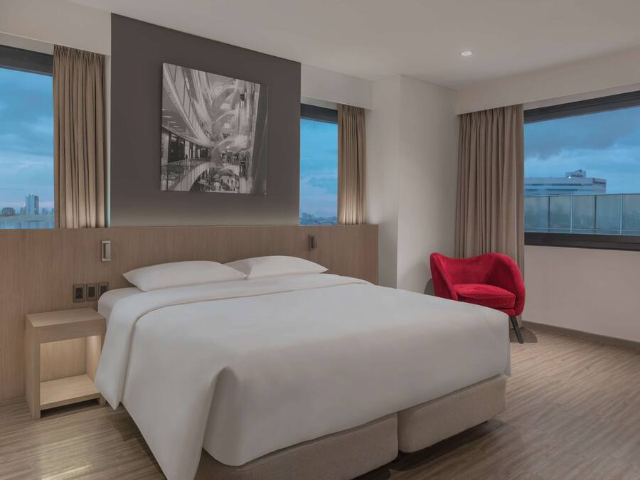 Un hotel moderno con una cama grande, una silla roja, vistas a la ciudad y un cuadro en la pared.