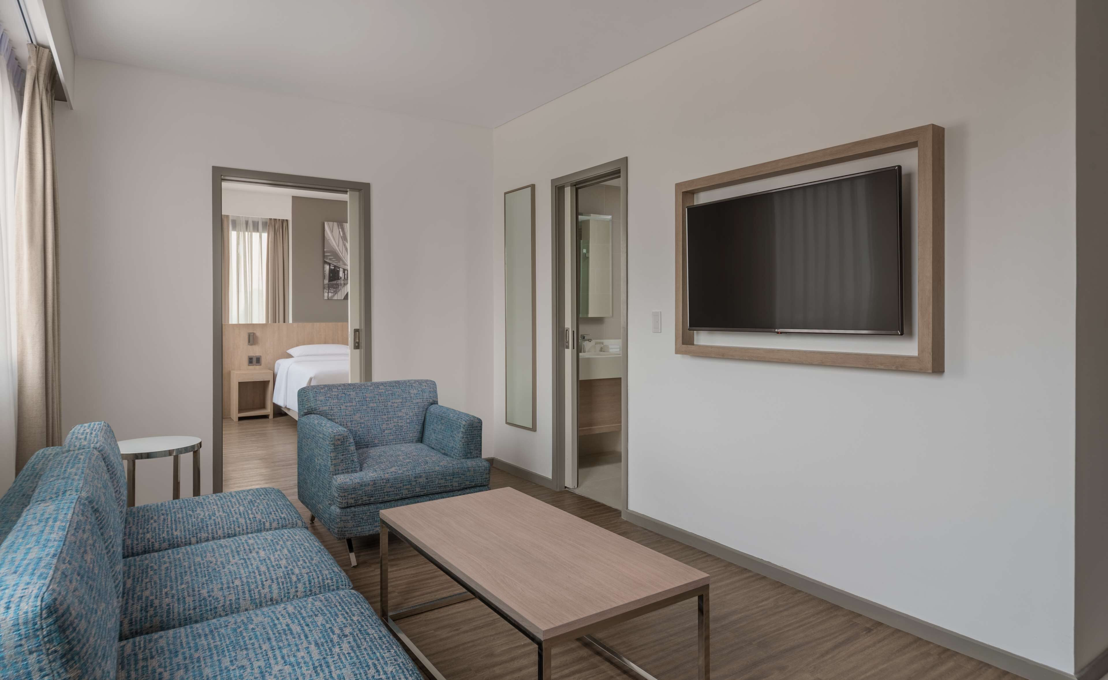 A hotel room with a bed, a seating area with two sofas, a small table, and a TV mounted on the wall.