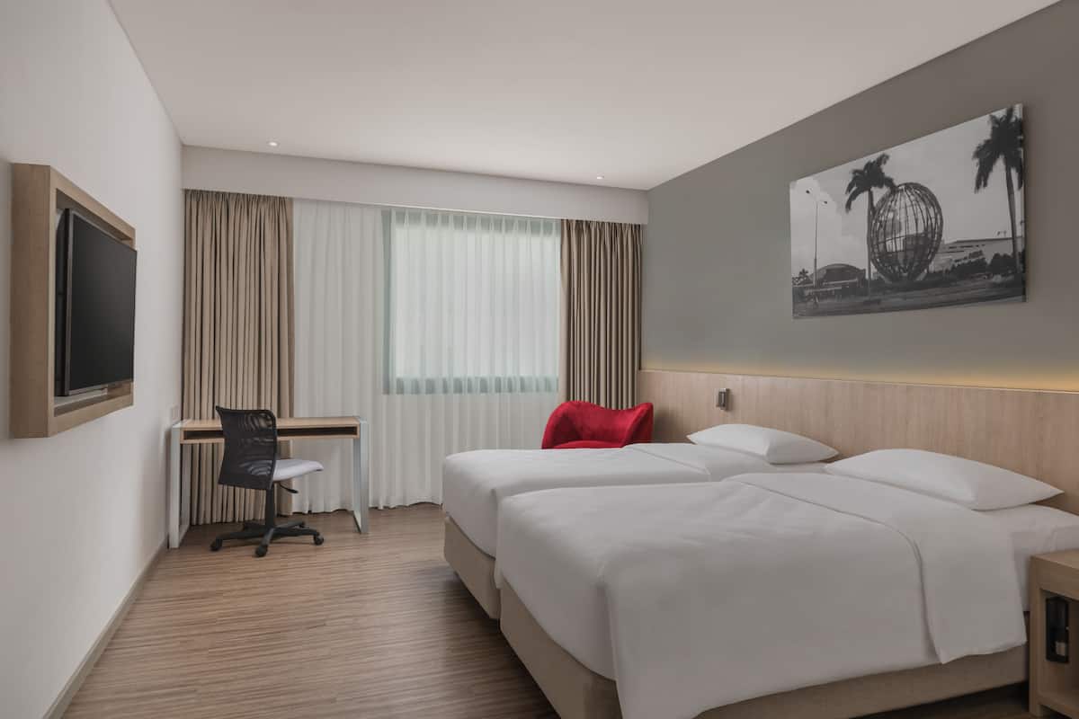 A hotel room with two beds, a desk, a chair, and a large window with curtains.