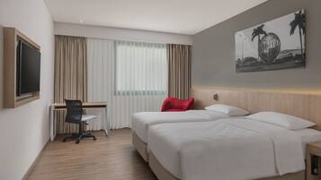 Habitación de hotel con dos camas, un escritorio, una silla y un ventanal con cortinas.