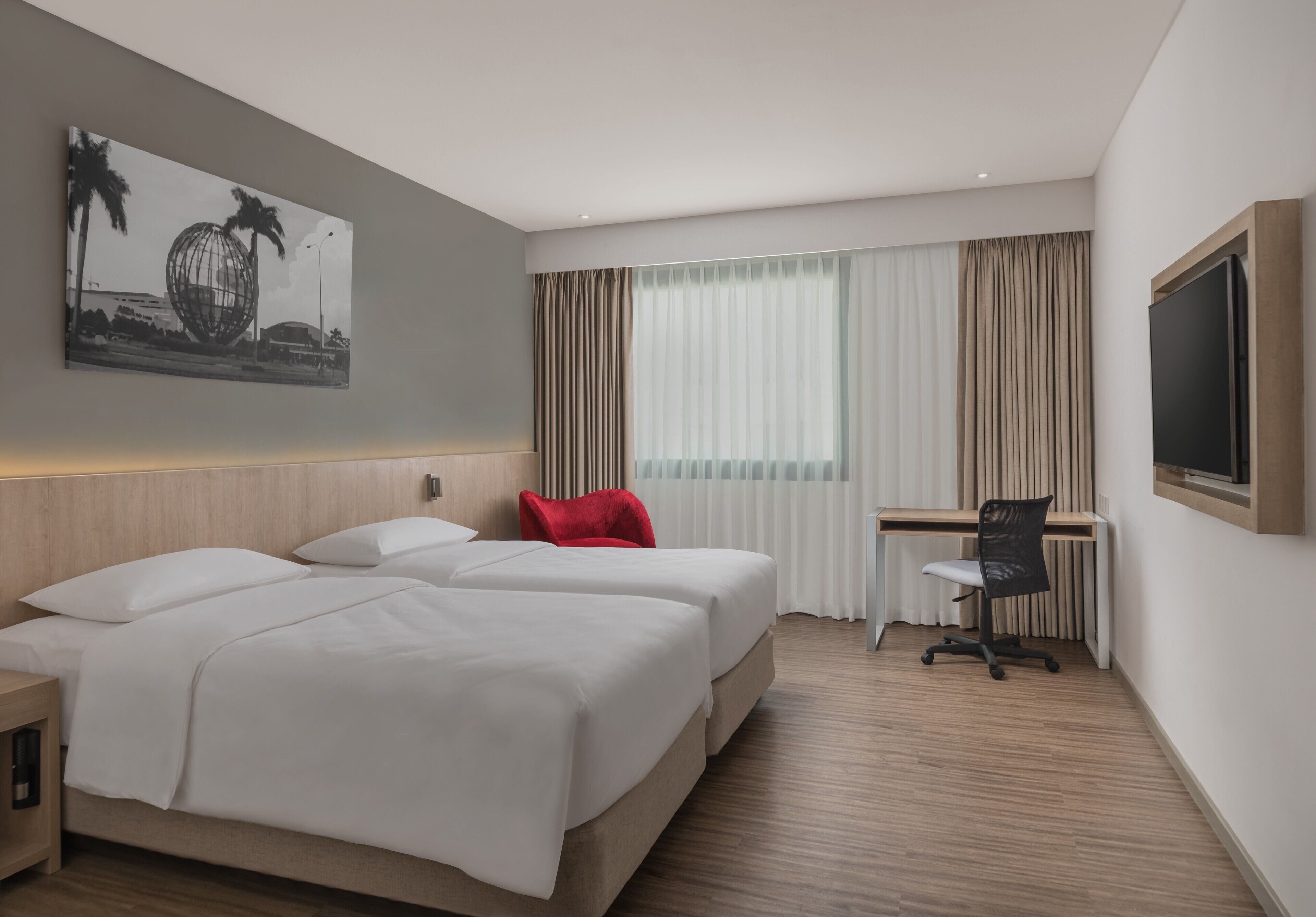 A hotel room with two beds, a desk, a chair, a TV, and a large window with curtains.