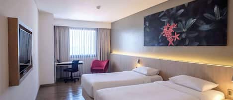 A hotel room with two beds, a desk, a chair, and a large floral artwork on the wall.