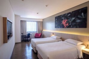 Habitación de hotel con dos camas, un escritorio, una silla y una obra de arte floral grande en la pared.
