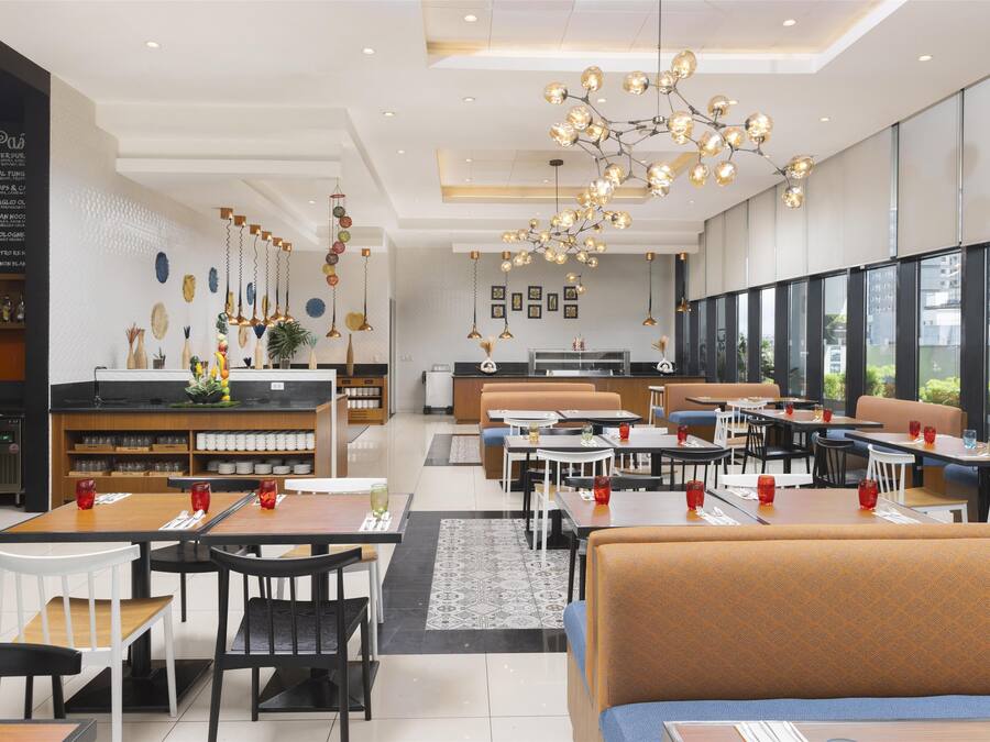 A modern restaurant with a central bar area, multiple seating options including booths and tables, and a large chandelier.