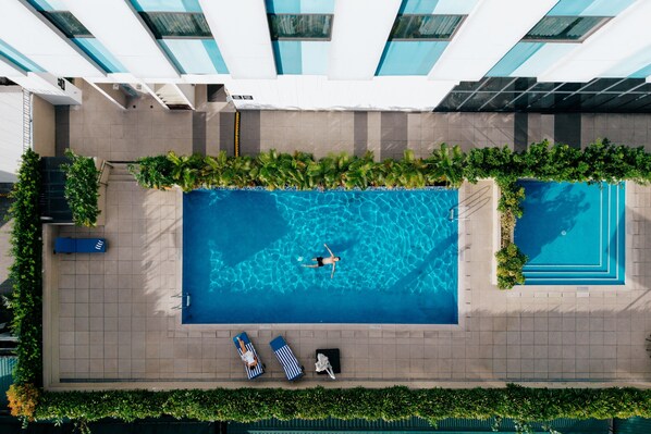 Vista aérea de una piscina en la azotea con dos tumbonas y una persona nadando.