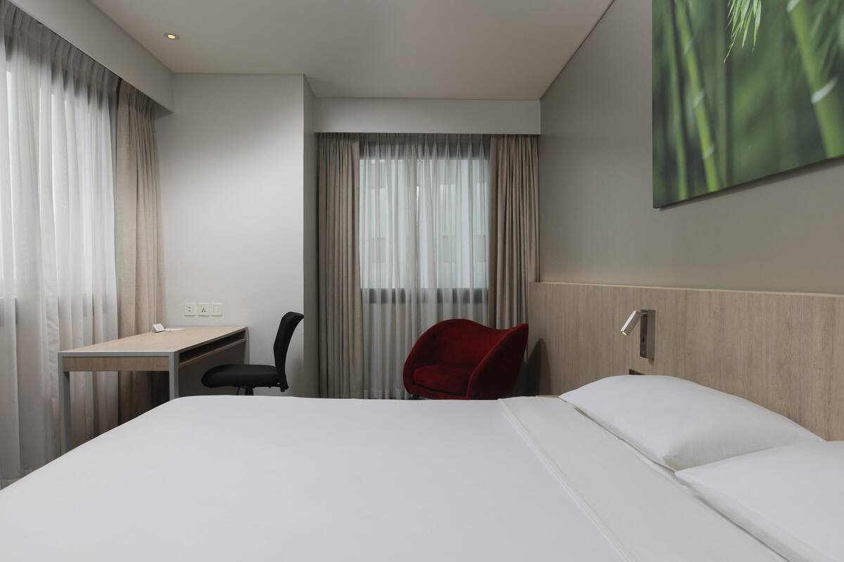 A hotel room with a bed, a desk, a chair, and a large window with curtains.