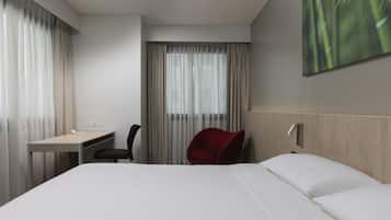A hotel room with a bed, a desk, a chair, and a large window with curtains.