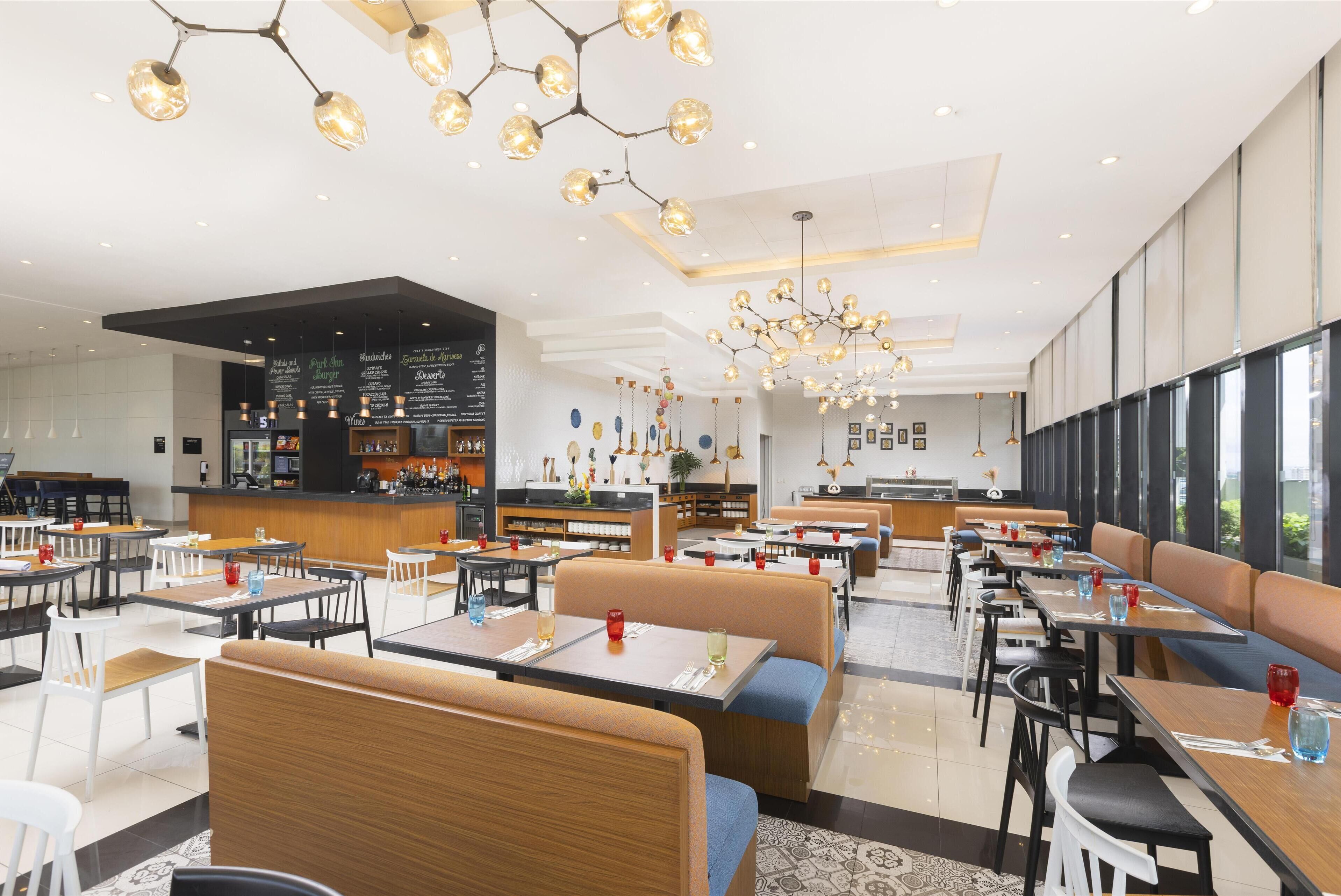 Ein modernes Restaurant mit mehreren Sitzbereichen, darunter Boxsitzgelegenheiten und Tische sowie einer Bar.