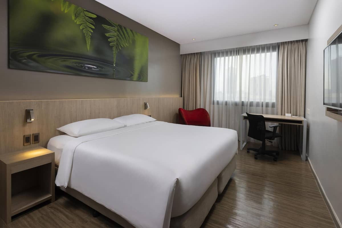 A hotel room with a large bed, a desk, a chair, and a painting on the wall.