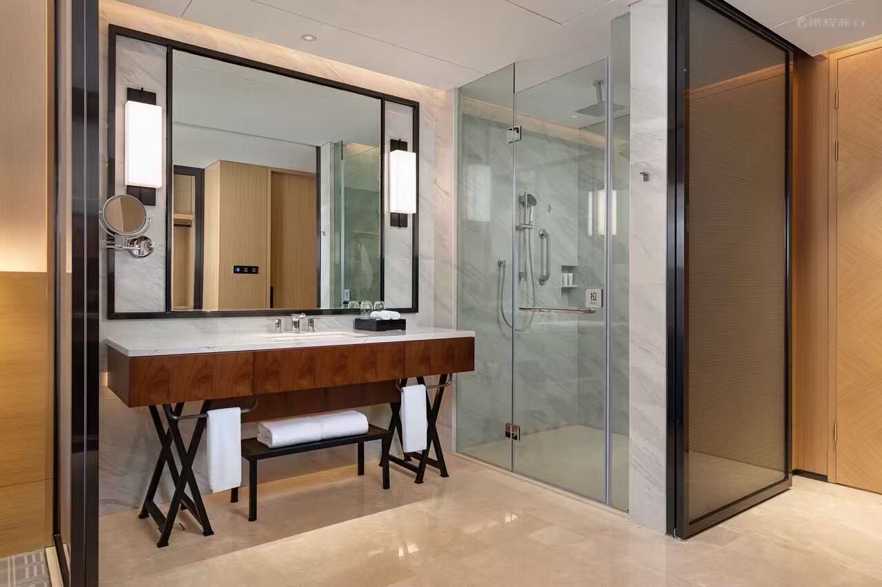 A modern bathroom with a large mirror, a wooden vanity, a glass shower enclosure, and a separate toilet area.