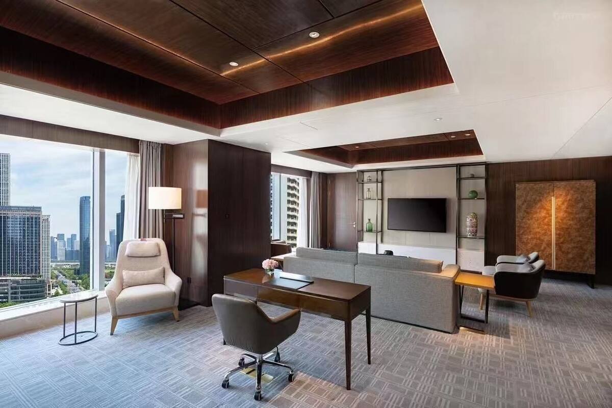 A modern hotel room with a large window, a desk, a sofa, and a TV.