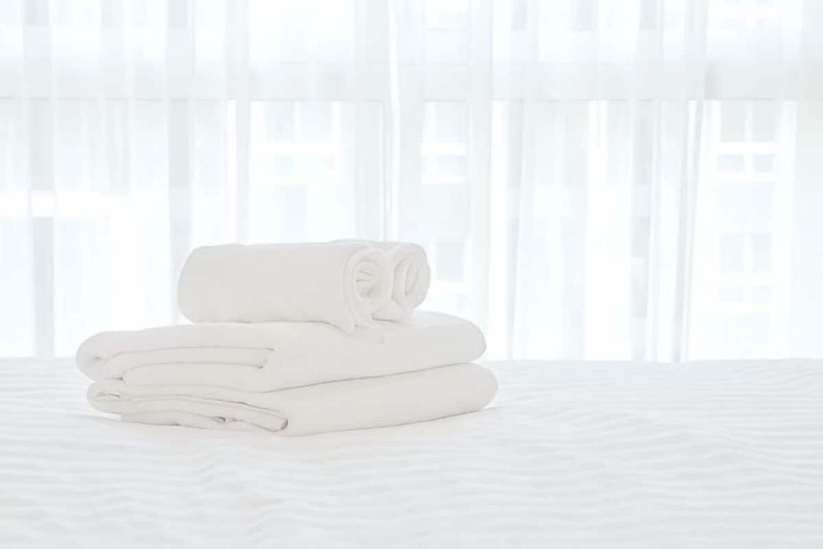 A neatly folded white towel on a bed with a sheer white curtain in the background.