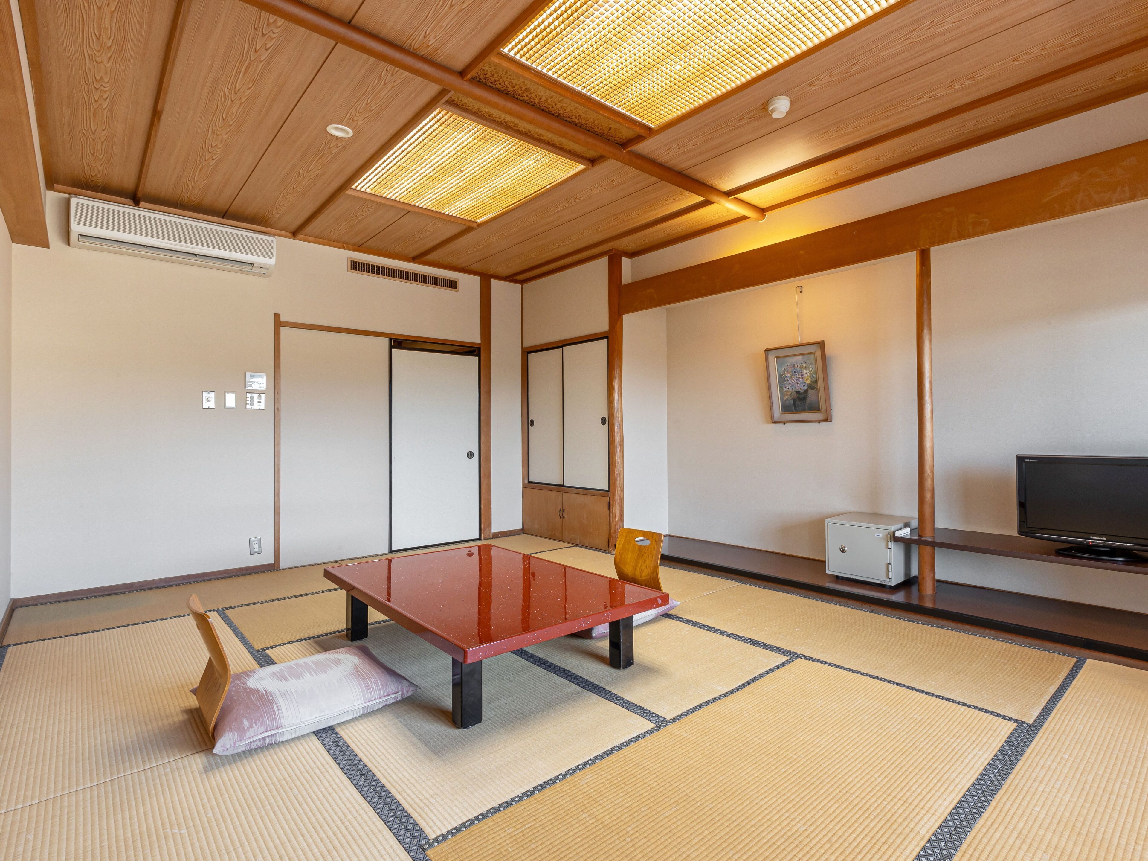 A traditional Japanese room with tatami flooring, a low table, a cushion, a television, and a painting on the wall.