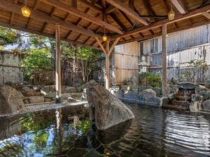 A traditional Japanese onsen with a wooden roof, stone basin, and bamboo wall. - KAMENOI HOTEL TSUKUBASAN (Tsukuba)