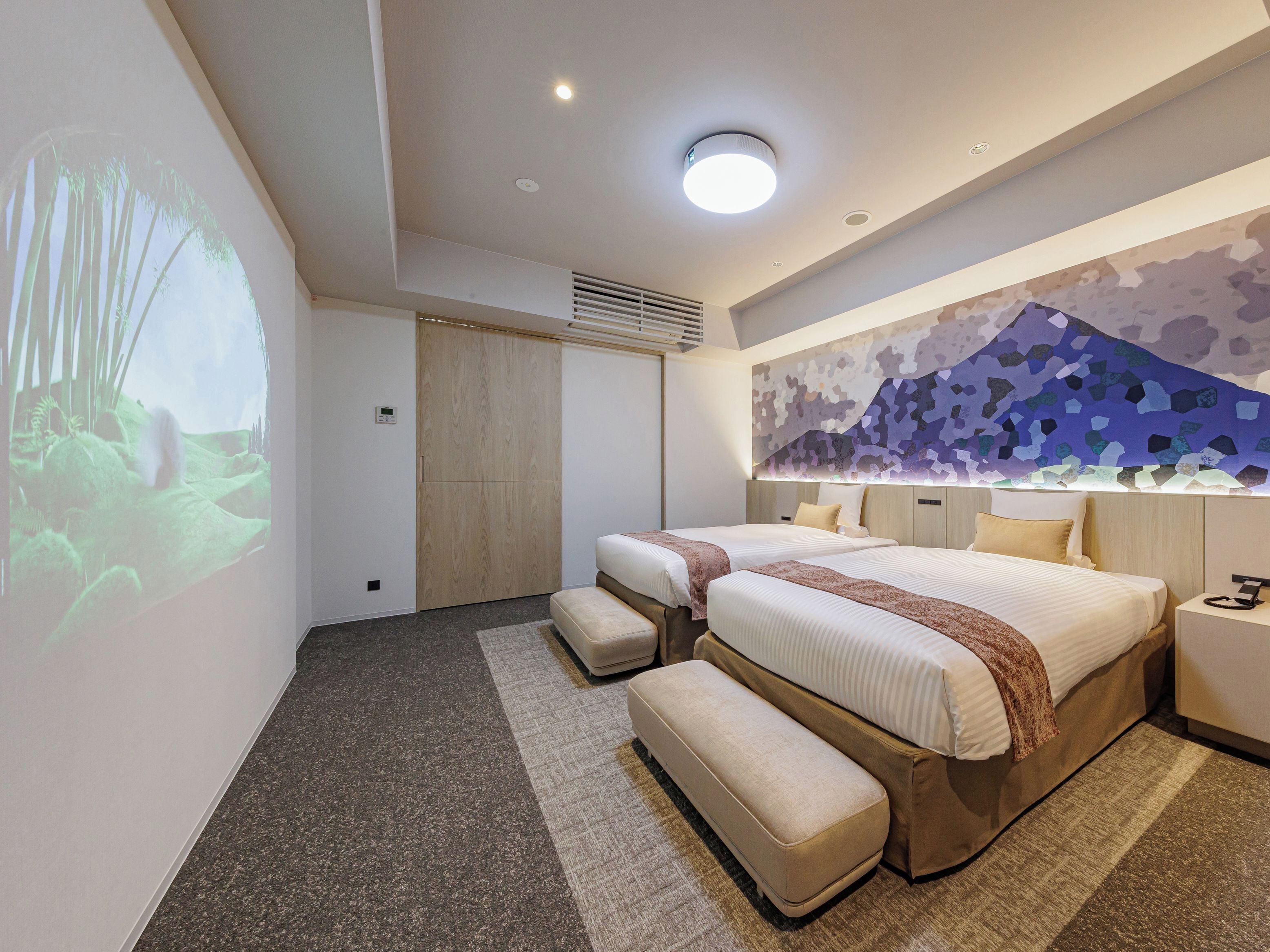 Una camera d'hotel moderna con due letti, una grande proiezione a parete e un design di soffitto originale.