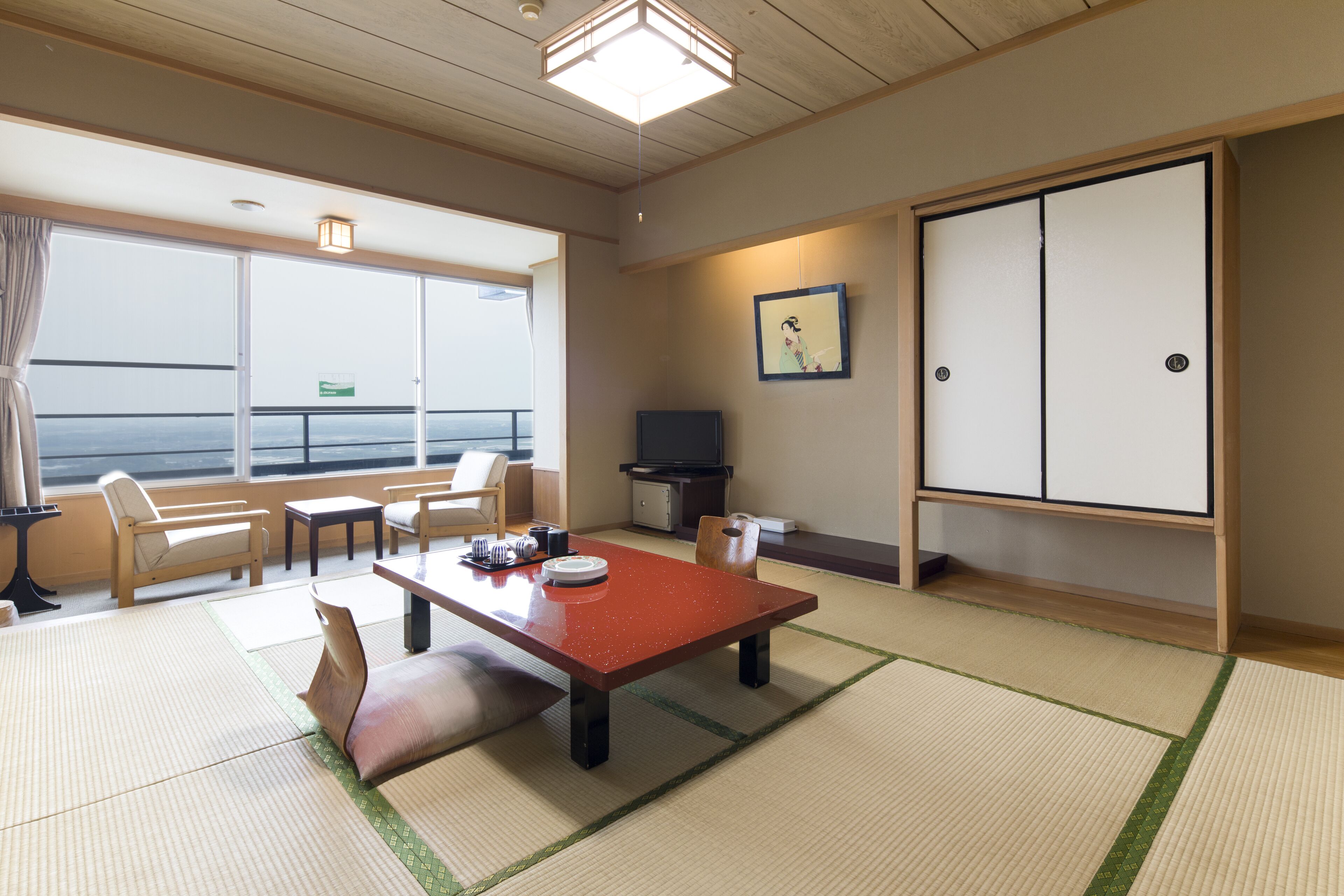 A traditional Japanese room with tatami flooring, a low table, chairs, a television, and a sliding door.