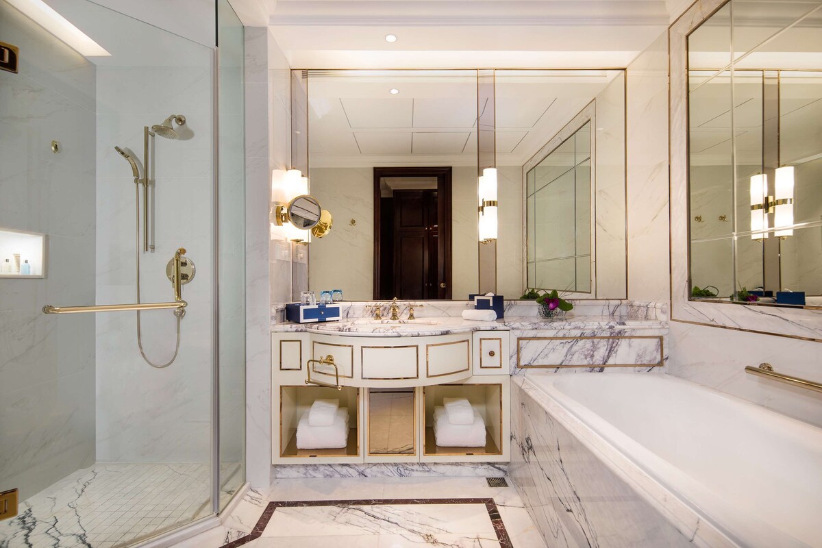 A luxurious bathroom with a glass-enclosed shower, a large mirror, and a marble-topped sink.