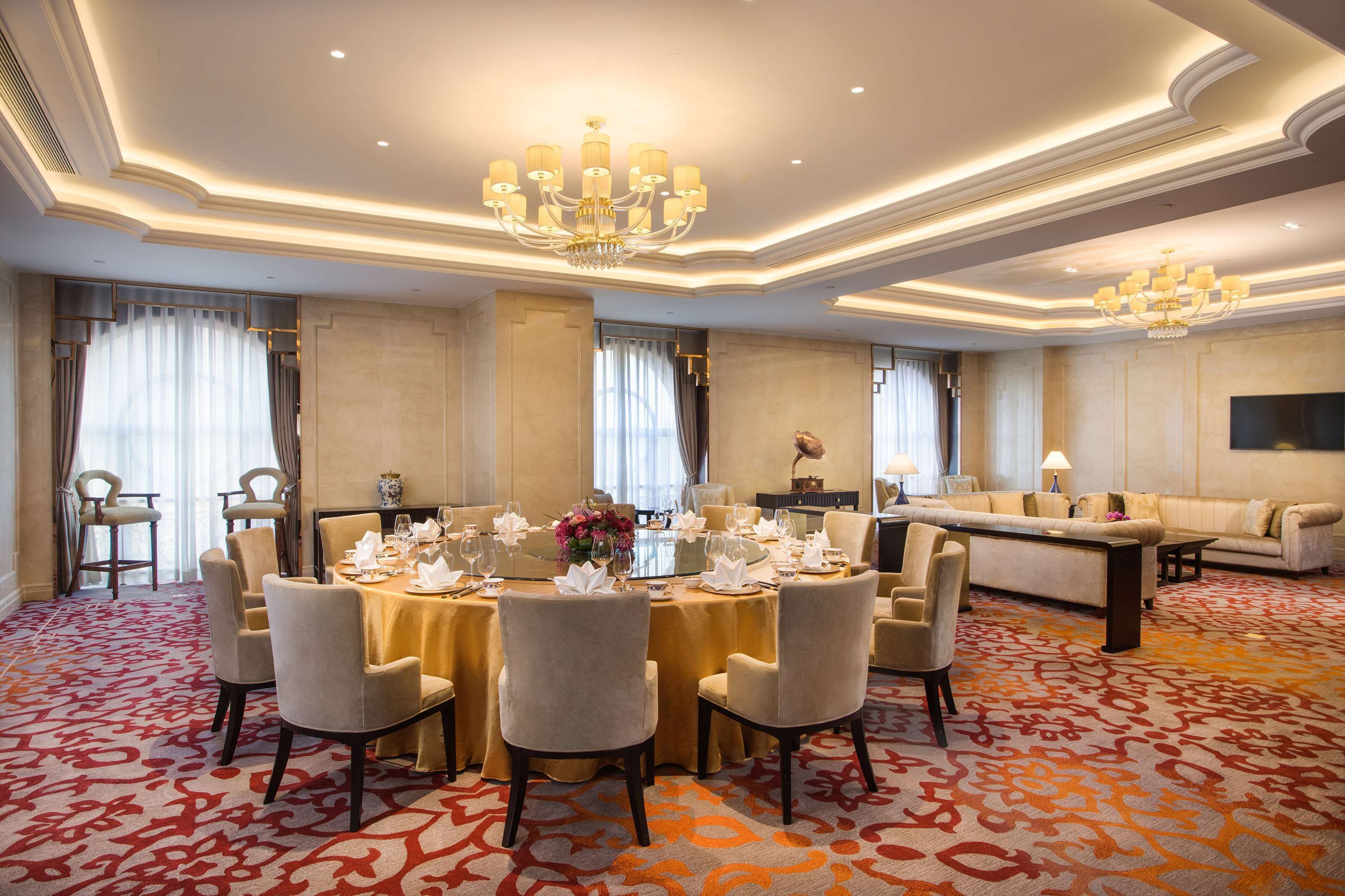 Une chambre d’hôtel spacieuse, dotée d’une grande table à manger dressée pour un repas, d’un canapé et d’un lustre.