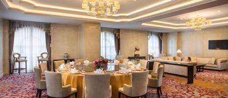 Une chambre d’hôtel spacieuse, dotée d’une grande table à manger dressée pour un repas, d’un canapé et d’un lustre.