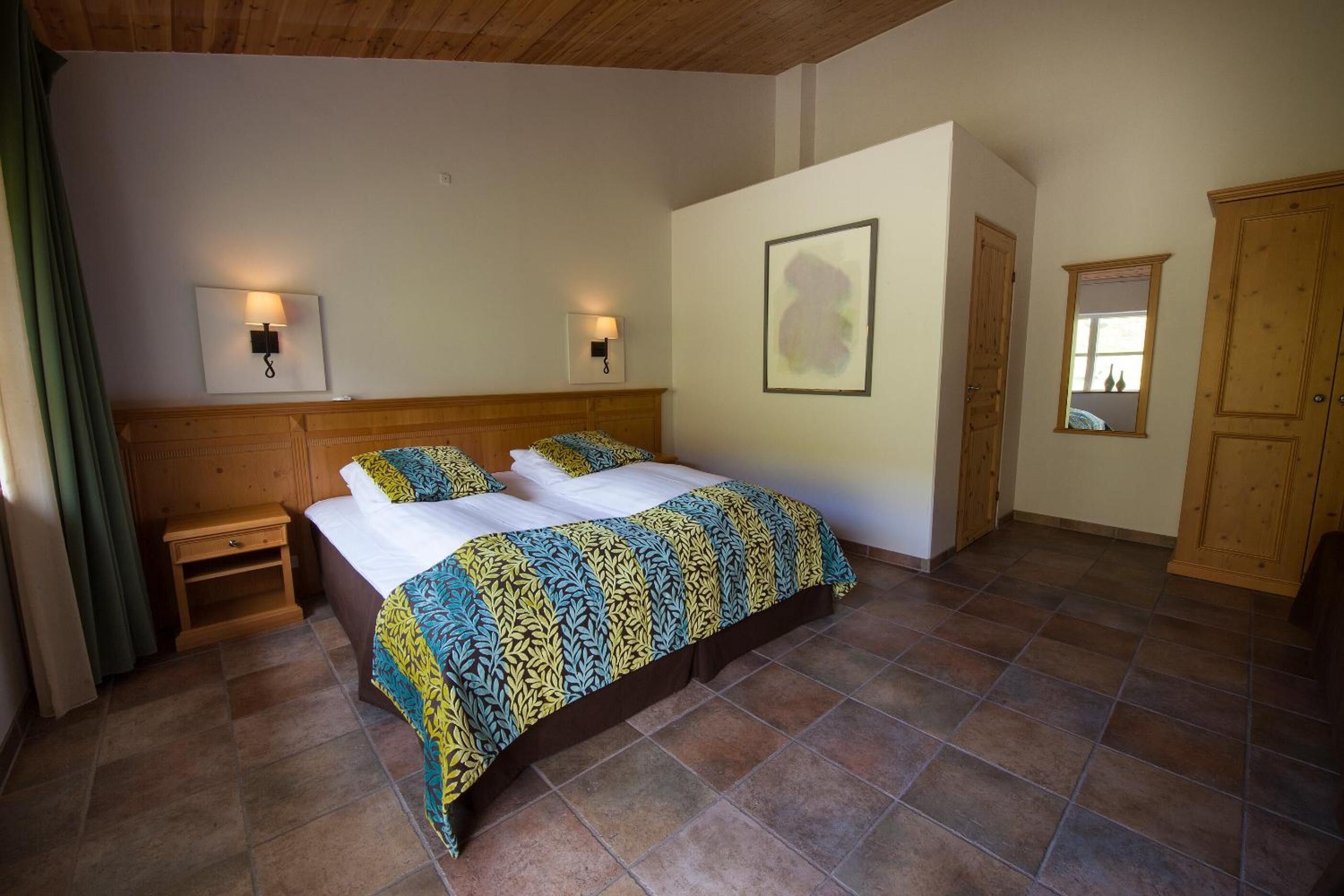 A bedroom with a bed, two bedside tables, a wooden wardrobe, and a wall-mounted light fixture.