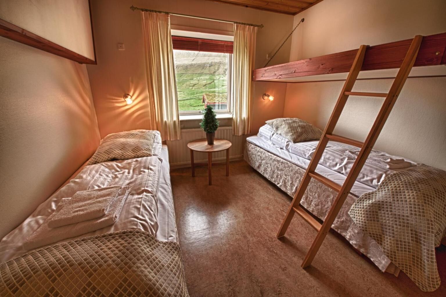 Ett litet, mysigt rum med två enkelsängar, ett litet bord och ett fönster med gardiner.