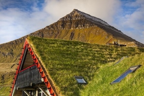 A mountain with a red-roofed structure and solar panels on a grassy slope. - Gjaargardur Guesthouse Gjogv (Gjogv)