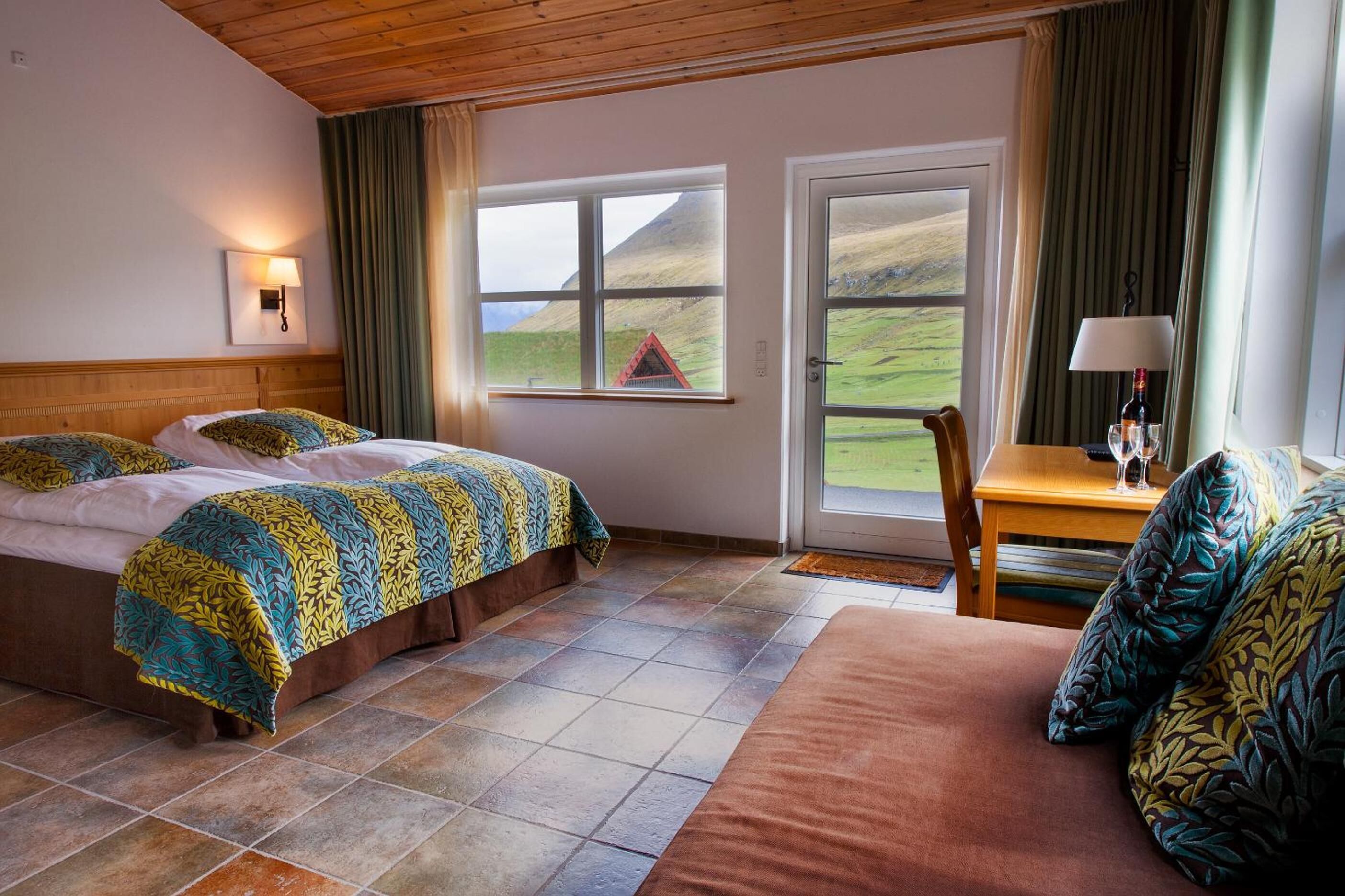 Une chambre d’hôtel avec deux lits, un coin salon et une fenêtre donnant sur une colline.