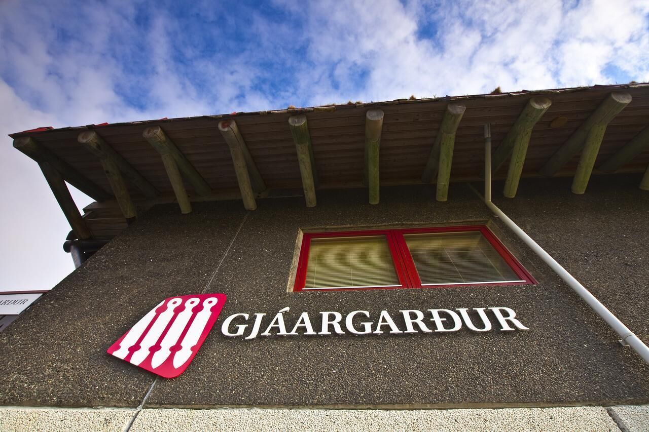 En byggnad med en skylt där det står ”GJAARGARDUR” och en röd och vit logotyp.